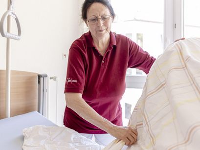 Frau bezieht Bettwäsche im Patientenzimmer